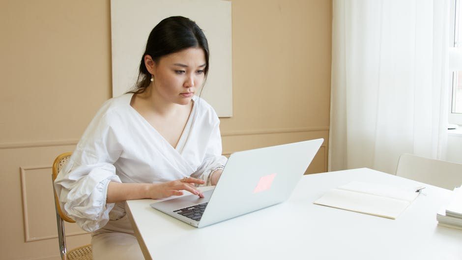 Professional woman focused on her work at a desk using a laptop in a bright office setting.