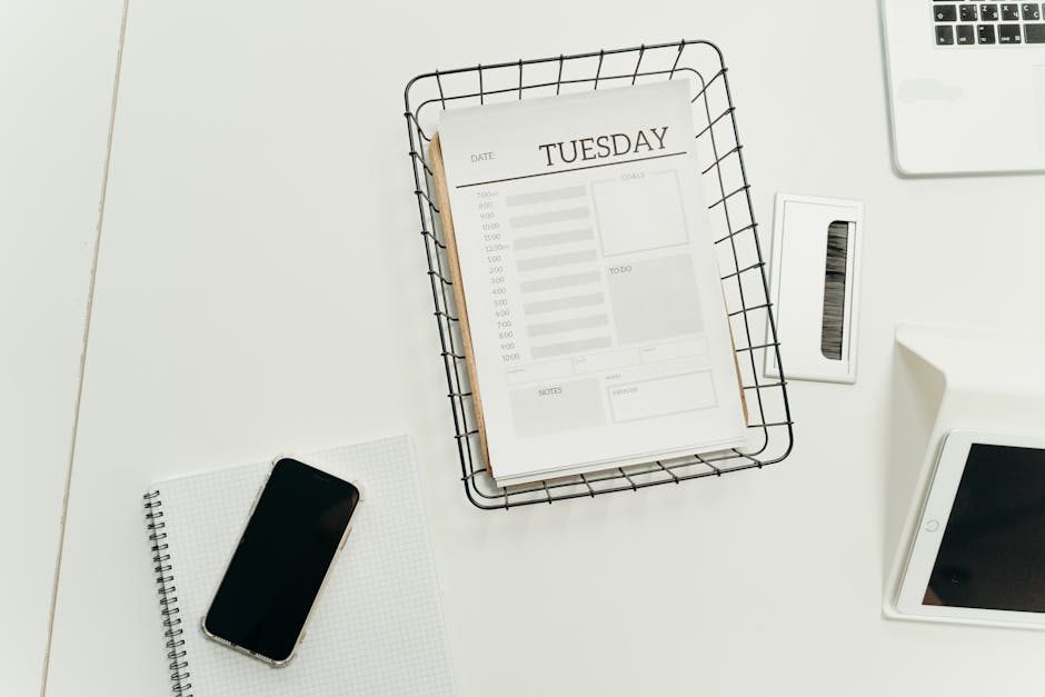 Top view of a neat office desk with a Tuesday planner, smartphone, and gadgets, perfect for scheduling and organization.