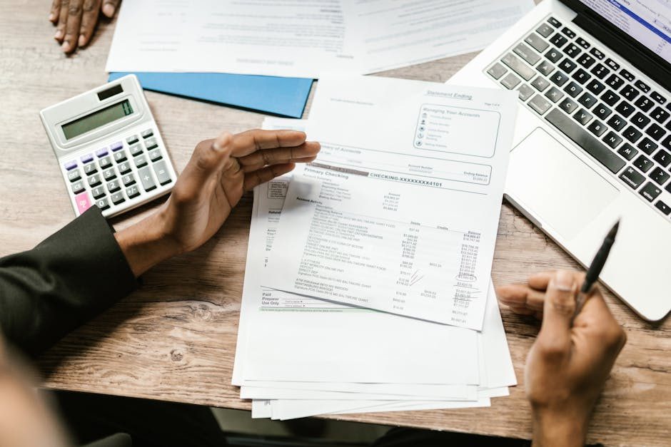 Close-up of hands organizing documents on a desk with a laptop.