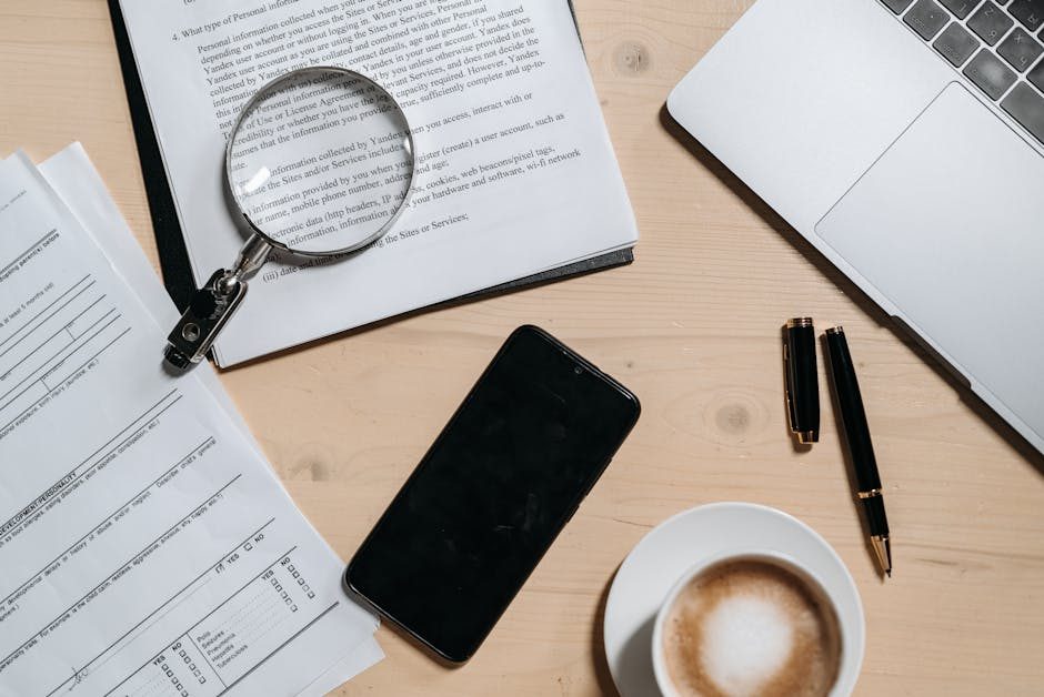 Top view of documents, laptop, coffee, and magnifying glass on office desk.