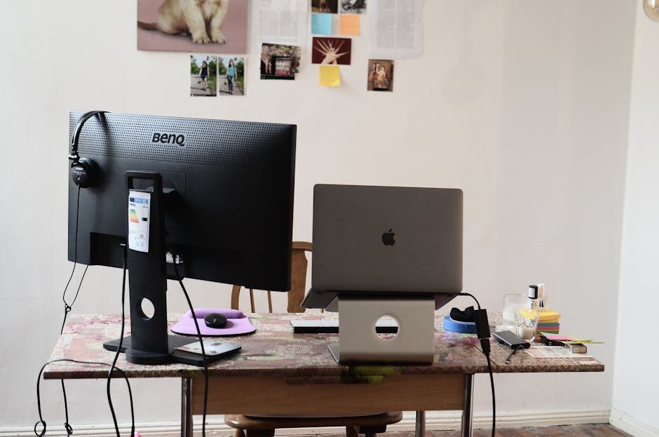 A chaotic office desk with a laptop, scattered papers, sticky notes, and a potted plant.